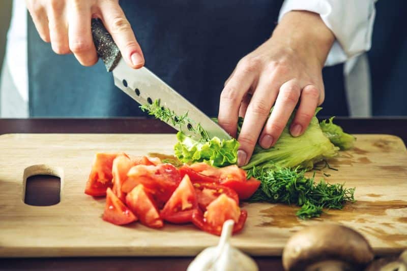 View of chef's hands cutting lettuce on a cutting board with tomatoes