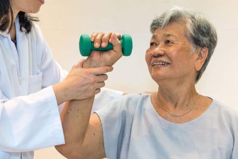 Physical therapist helping patient lift a small dumbbell